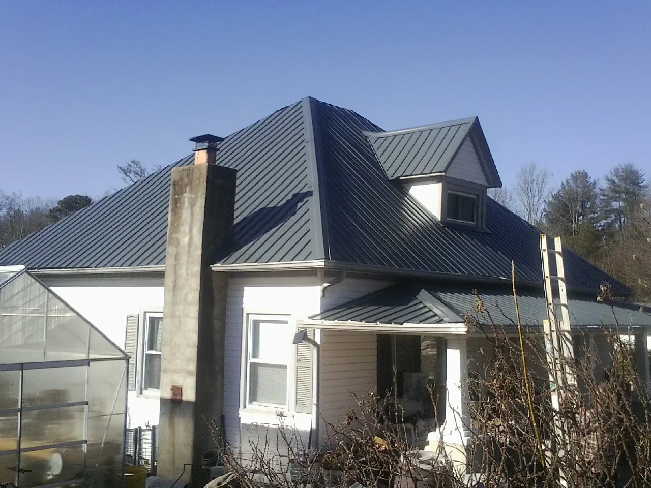 Dark blue standing seam metal roof on a white farmhouse with dormer — Slate & Tile Roof Repair by Roofing Brothers in Glidden