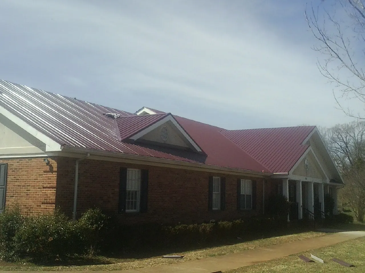 Red metal roof with gabled entries on a long brick building, from a Hail Damage Roof Repair job in Glidden