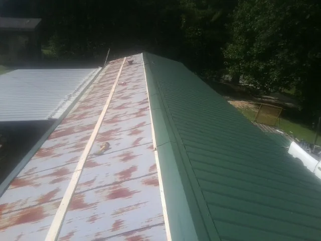 Old rusted panels beside newly installed green metal roofing — Wind Damage Roof Repair by Roofing Brothers in Glidden