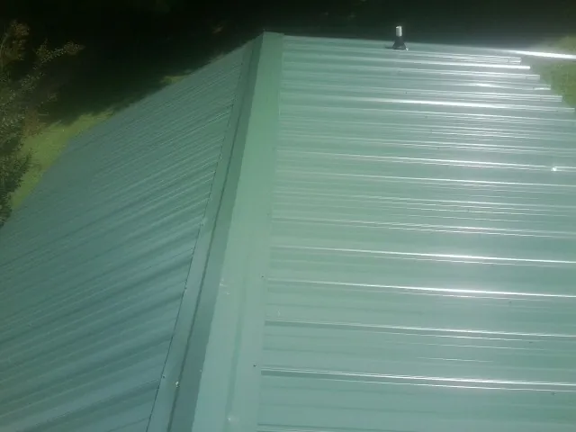 New green metal panels meeting at the ridge of a roof — Flat Roof Repair work by our crew in Glidden