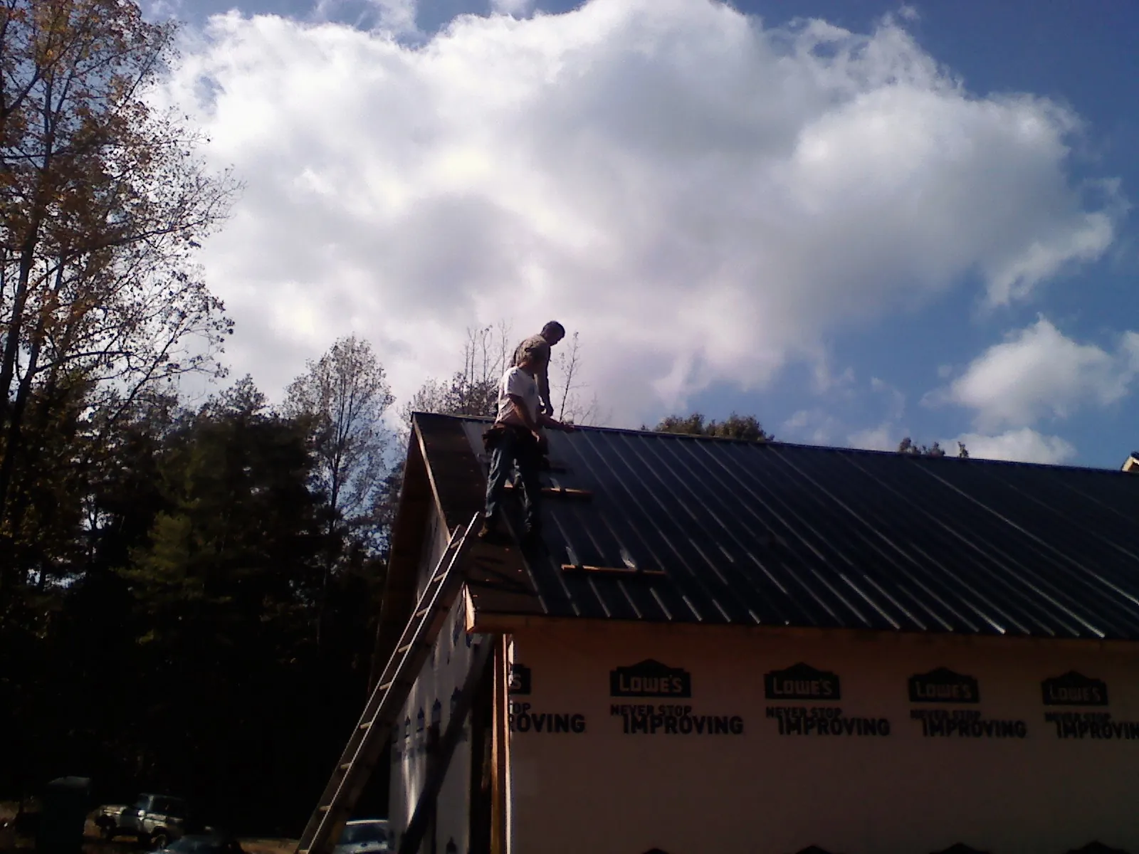 Roofer fastening dark metal panels high against a cloudy sky, from a Roof Inspection job in Glidden