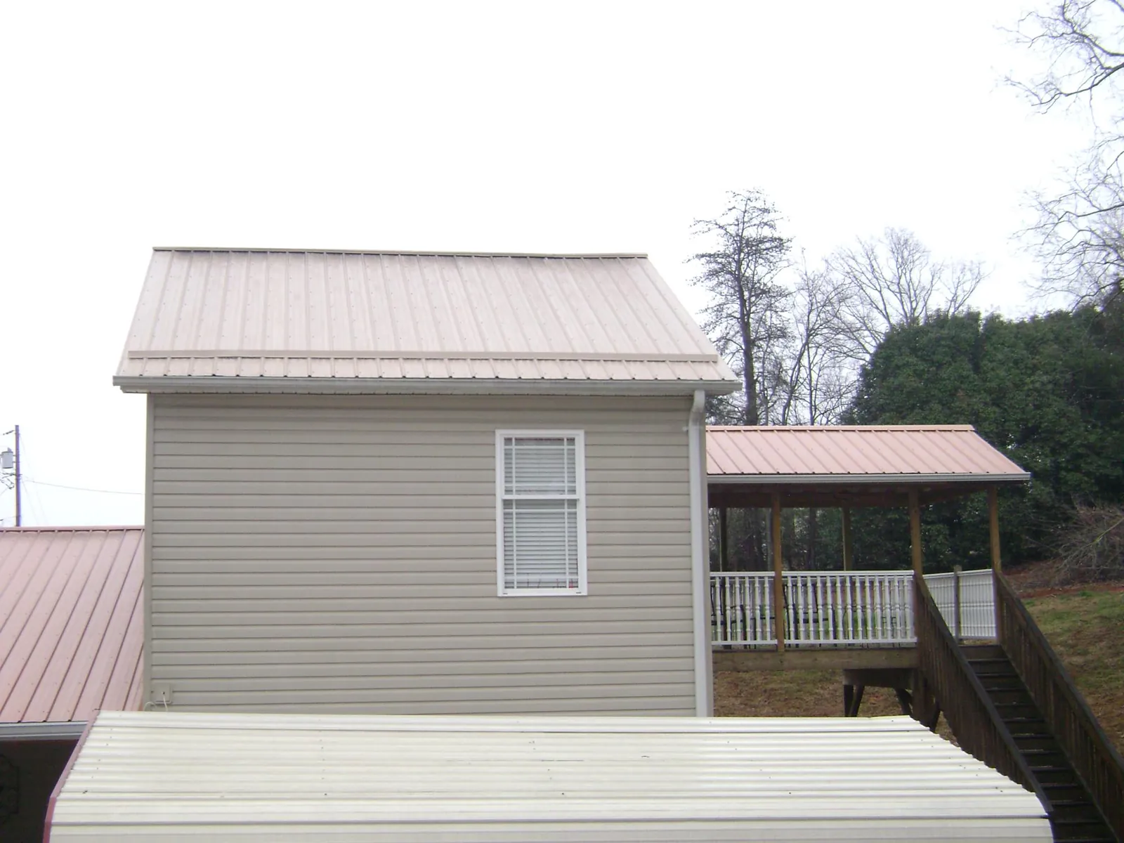 Tan metal roofs on a two story addition and attached porch, from a Roof Replacement job in Glidden
