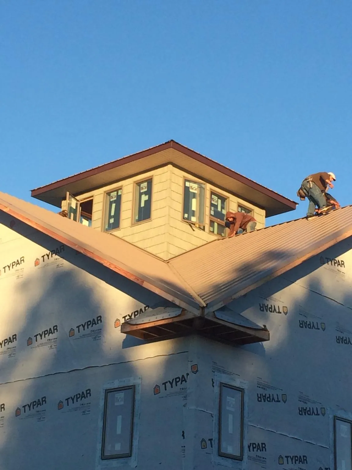 Roofers working around a rooftop cupola on a new metal roof at sunset — Roof Waterproofing in Glidden by Roofing Brothers